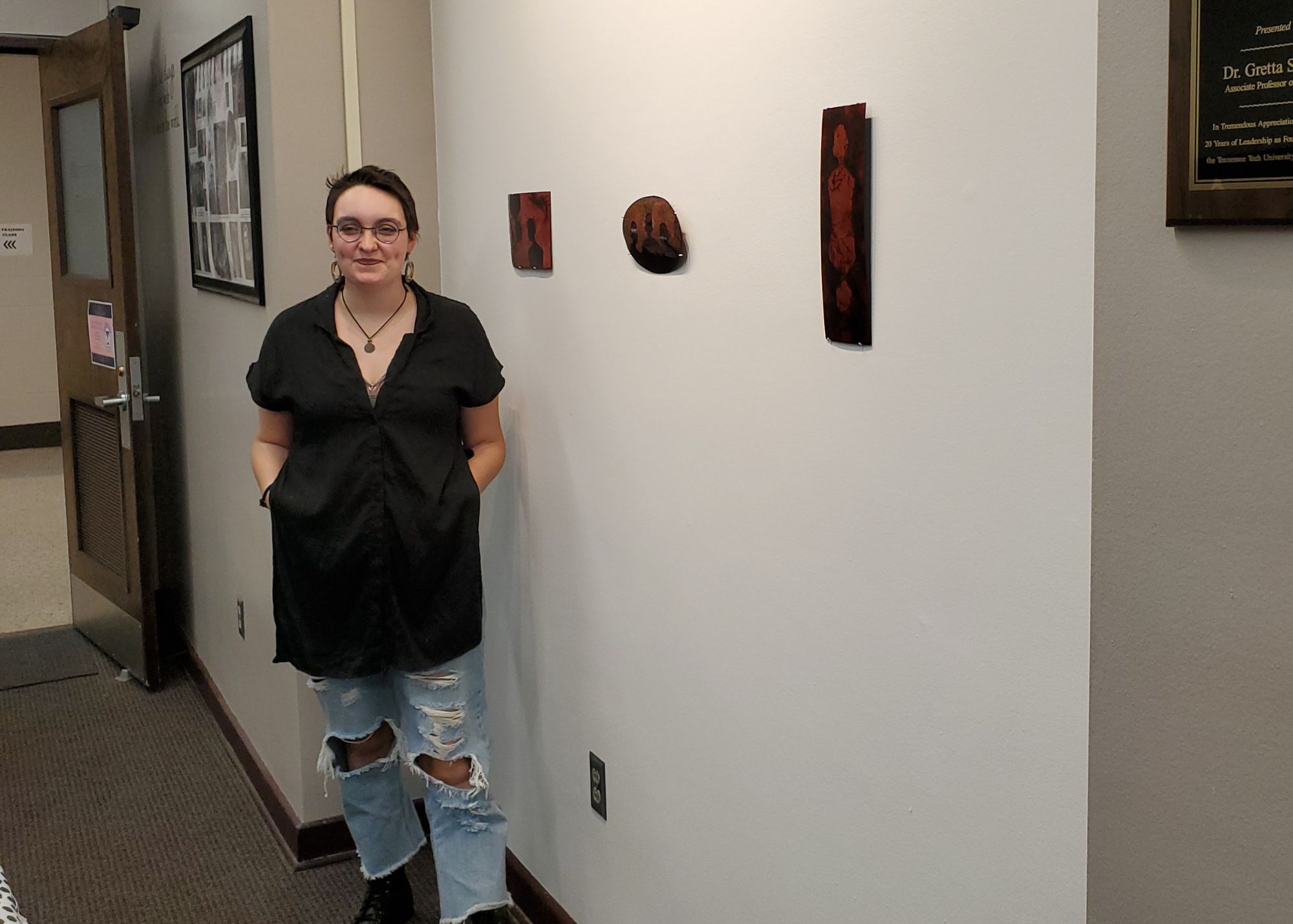 This is a picture of Anna Grayson standing in front of her artwork at the Women's Center's new gallery space.